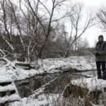 Wildnispädagogin in verschneiter Winterlandschaft am Wasser - Treffen im Winter mit der WildnisGemeinschaft
