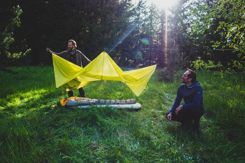Zwei Männer bauen ein Tarp auf einer Wiese auf - Sommer erleben mit der WildnisGemeinschaft